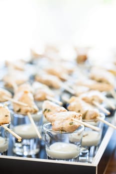 Closeup of pieces of cooked chicken on wooden skewers with mayonnaise based condiment in small glasses