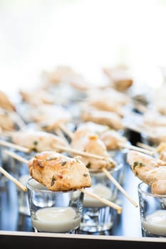 Closeup of pieces of cooked chicken on wooden skewers with mayonnaise based condiment in small glasses
