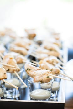 Closeup of pieces of cooked chicken on wooden skewers with mayonnaise based condiment in small glasses