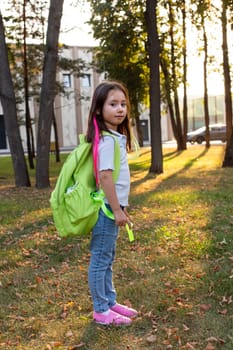 Young girl with backpack in sunlit park landscape, look at camera.