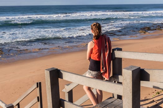 Girl teenager daughter overlooking landscape ocean beach sand rock reefs pools at low tide from stairs