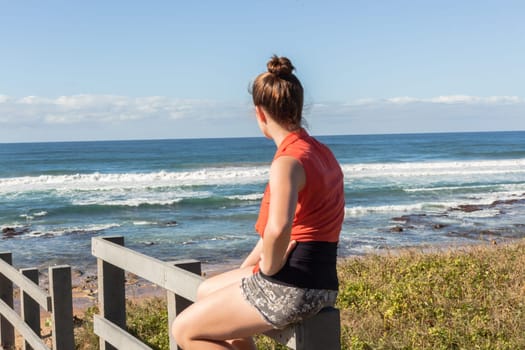Girl teenager daughter overlooking landscape ocean beach sand rock reefs pools at low tide from stairs