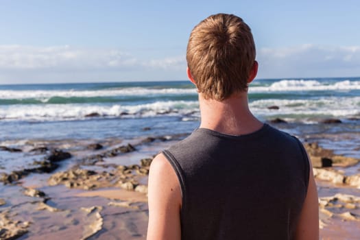 Boy unidentified rear photo overlooking ocean beach sand rock reefs pools at low tide