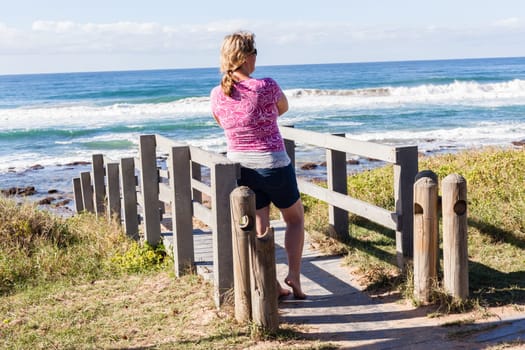 Woman overlooking landscape ocean beach sand rock reefs pools at low tide from stairs