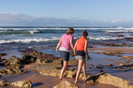 Girls mother daughter together exploring ocean beach rock reefs pools at low tide