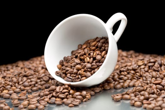 Coffee beans spilled out of coffee cup. On black background.
