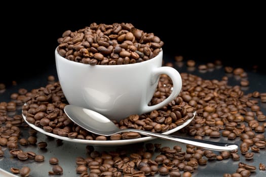 Cup and saucer full of coffee beans with a spoon on a black background