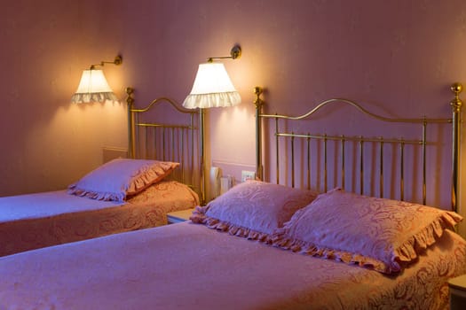 Trendy hotel in pink with two beds, in the light of the bedside lights and cold light from the window.