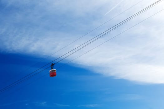 Red cable car cabin in the sky with clouds.