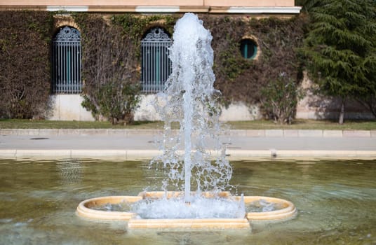 Fountain in the park on a background of the fence.