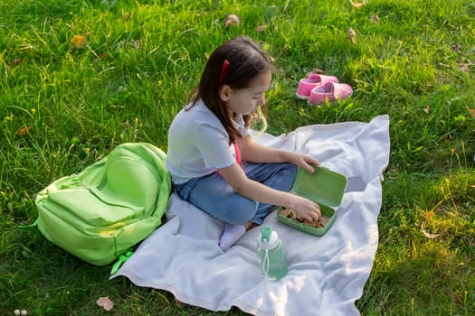 Child enjoying picnic in park with healthy lunch and backpack on grass.