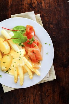 Delicious cold summer dinner of parma ham and white asparagus spears topped with tangy mayo and served with boiled baby potatoes, overhead view on a dark background