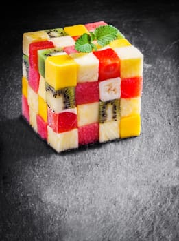 Colorful gourmet cube of diced fresh tropical fruit with watermelon, melon, orange, strawberry, banana, kiwifruit and apple garnished with mint on a slate kitchen counter with copyspace