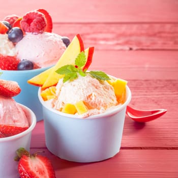 Individual servings of cool refreshing ice-cream topped with fresh tropical fruit including apple, strawberries, blueberries and raspberries, square format with copyspace