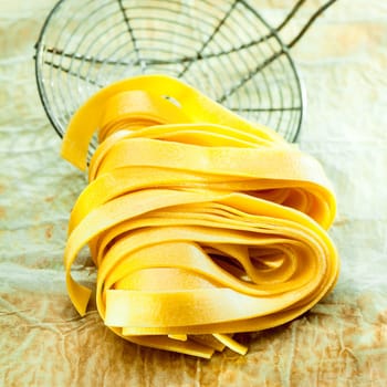 Closeup of coiled Italian fetuccine pasta ribbons with an old wire kitchen strainer in the background