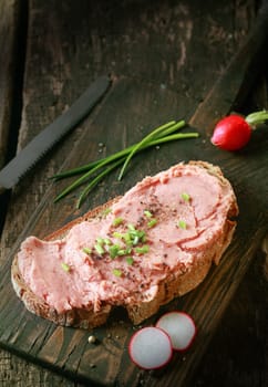 Delicious wholesome German cuisine with a slice of rye bread topped with a spread of smoked pork and bacon teewurst being prepared with fresh chopped chives, spices and radish, high angle view