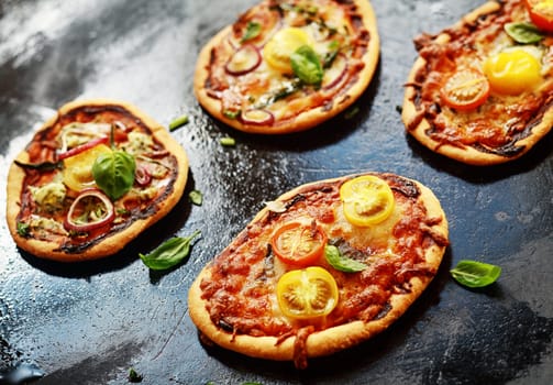Selection of mini Italian vegetarian pizzas topped with cheese, onion, tomato and basil in a cafeteria or pizzeria for a tasty midday snack