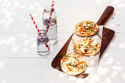 A trio of tasty mini vegetarian pizzas with eggplant, bell pepper, cheese and herbs served on a long wooden board with glass jars of fresh water