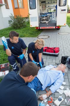 Paramedics treating injured senior man lying on street