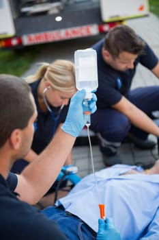 Paramedic team preparing drip for injured patient lying on street