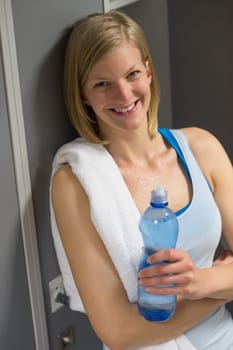Sweaty woman with bottle and towel in locker room at gym