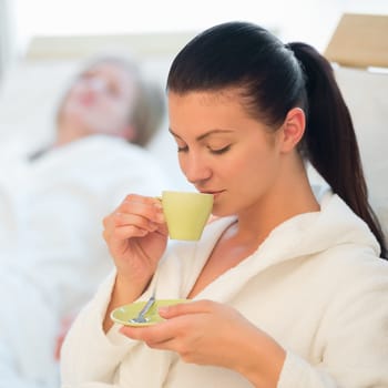 Young woman drinking coffee at spa with friend in background
