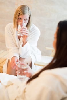Young woman drink water with friend at beauty spa