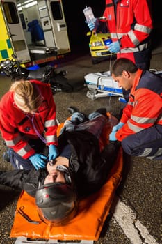 Paramedics examining injured motorcycle man driver on road at night
