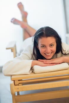 Happy woman relaxing on wooden bed at beauty spa