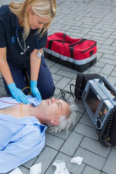 Paramedic examining unconscious elderly patient lying on street