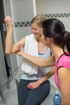 Young woman checking friend's muscles in changing room at gym