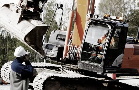 worker and driver operating large bulldozer, digger inside construction site