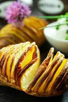 Finely sliced foil baked potato in the skin from a summer barbecue ready to be served with chopped chives and sour cream, close up view of the potato