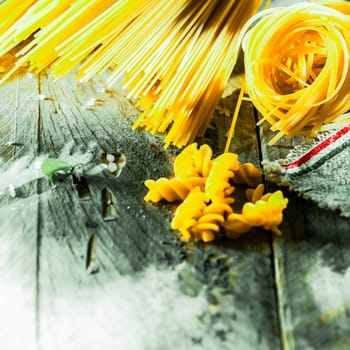 Assorted dried Italian pasta lying on old weathered wooden boards with spaghetti, fusilli, and linguini