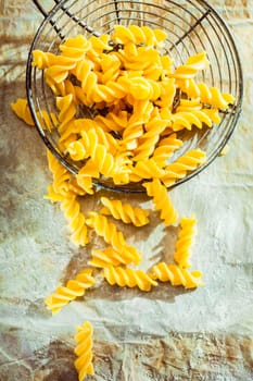 Old wire kitchen strainer filled with Italian fuilli pasta with its distinctive spiral shape said to lock in the flavor, overhead view during preparation of a tasty pasta dish