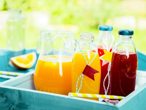 Healthy freshly squeezed fruit juice with bottles of orange citrus blend and fresh berry juice standing on a turquoise picnic table in a summer garden