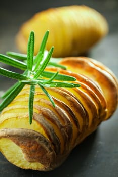 Baked potato cooked in foil on a barbecue and sliced through served with a sprig of fresh rosemary, close up vertical view