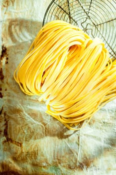 Overhead view of colied dried Italian linguine or tagliatelli egg noodle pasta lying with an old wire strainer on grunge paper with copyspace