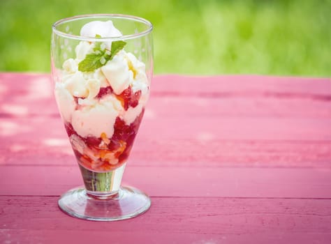 Strawberry pavlova dessert served in a tall glass on a summer picnic table outdoors with fresh strawberries, meringue, cream and ice cream for a delicious refreshing party treat