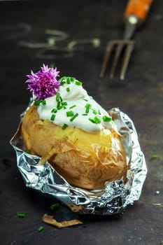 Foil baked jacket potato served in the aluminium foil wrapper topped with sour cream and fresh chopped chives and garnished with a purple chive flower