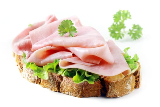 Delicious thin gourmet cured ham slices on crusty rye bread with fresh lettuce and parsley on a white background