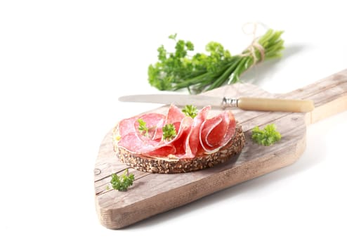 Preparing a delicious salami sandwich on crusty rye bread chopping a bunch of fresh parsley as a garnish, on an old wooden chopping board on white