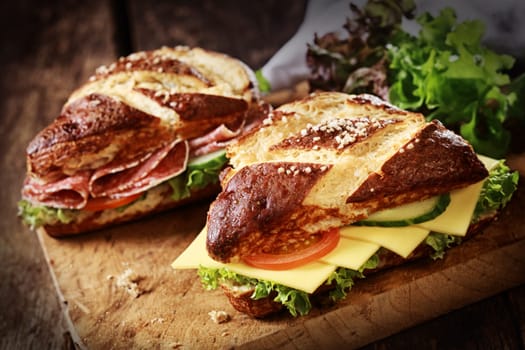 Lye bread rolls , a German and Bavarian speciality bread glazed and baked with lye, with cheese and salami with fresh lettuce, tomato and cucumber on an old wooden board
