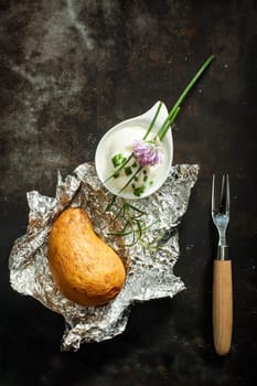 Baked jacket potato cooked over a summer barbecue in aluminium foil served with fresh chopped chives and sour cream for a delicious appetizer, overhead view