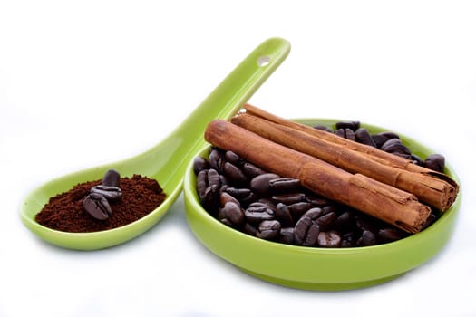 A green ceramic spoon and saucer with coffe beans and cinnamon on a white background