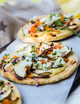 Mini vegetarian pizza with a golden crust topped with eggplant, cheese, herbs and bell peppers arranged in a row at a restaurant or takeaway