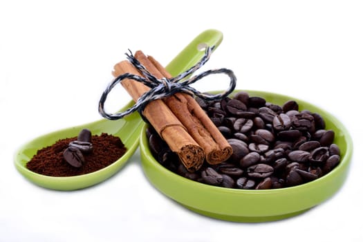 A green ceramic spoon and saucer with coffe beans and cinnamon on a white background