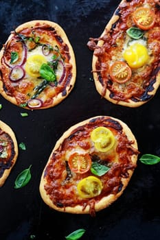 Savory mini Italian pizzas with cheese and tomato or onion, cheese and tomato toppings garnished with fresh basil, high angle view