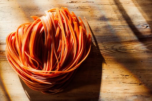 Tomato flavoured Italian tagliatelli or linguine pasta standing ready to be added to a savory pasta dish on an old wooden kitchen counter in dappled sunlight