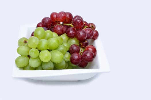 Bunch of red and green grapes on a white ceramic saucer